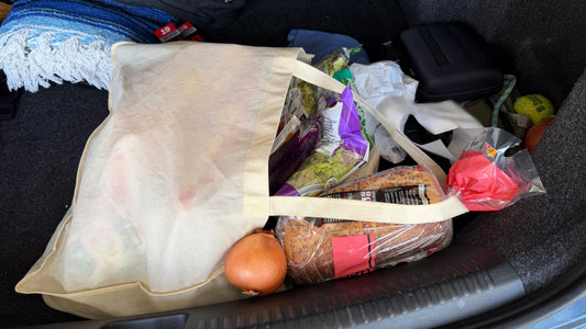 A bag of groceries that has spilled in the trunk of a car. Bread, produce and more is scattered throughout the trunk.